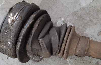Split and perished CV boot still on a removed driveshaft, with grease thrown out along the shaft