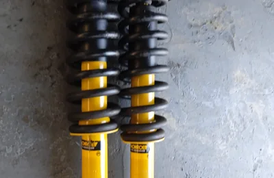 Two new shocks with coil springs fitted, laid out on the workshop floor