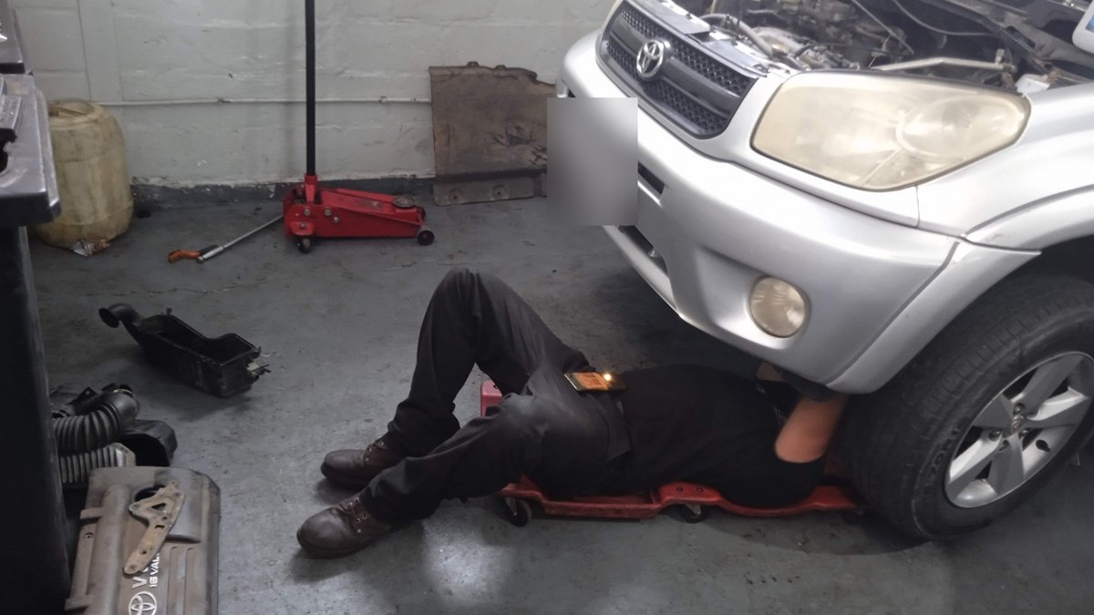 Mechanic servicing a car from underneath in the workshop