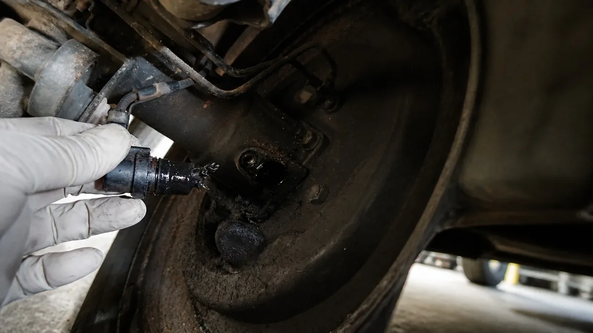 Mechanic holding a removed ABS wheel speed sensor beside its mounting point