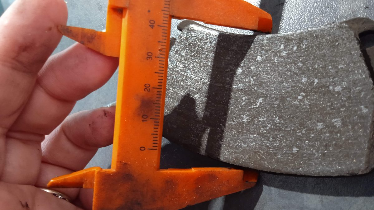 Vernier caliper measuring the friction material left on a worn brake pad