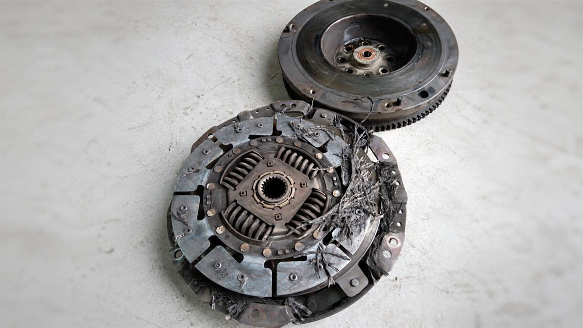 Destroyed clutch disc with shredded lining next to a flywheel