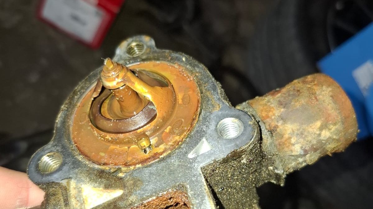 Corroded thermostat sitting in a housing full of rust sludge