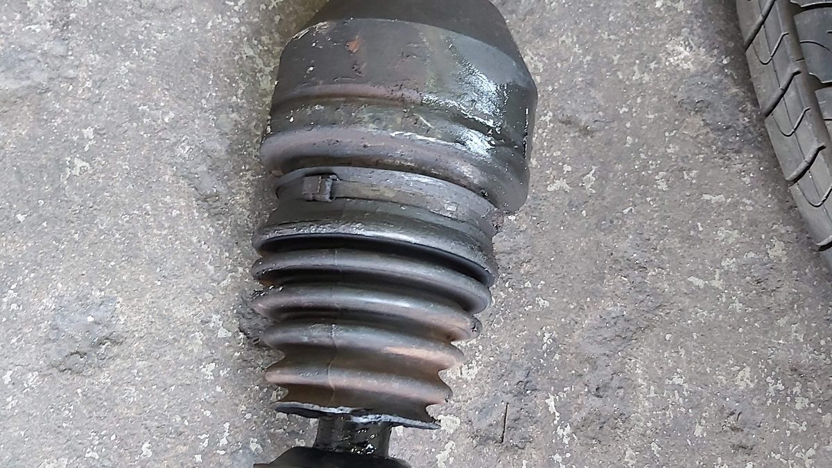 Car driveshaft removed showing the outer CV joint with a torn boot