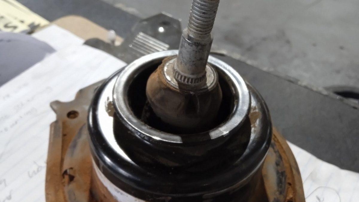 Worn hydraulic engine mounting removed from a car, sitting on a workshop bench