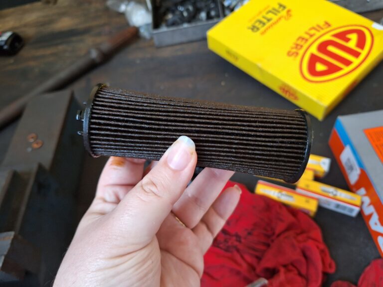 Used oil filter cartridge with new filters and spark plugs on a workshop bench at Fangio Hermanus