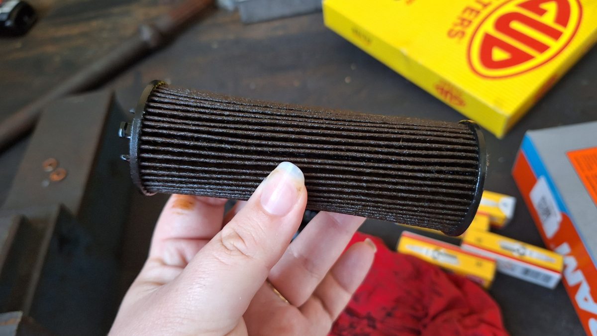 Dirty cartridge oil filter held up on a workshop bench next to a new filter box